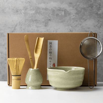Tea-making set with green bowl, whisk, and other tools against a gray background