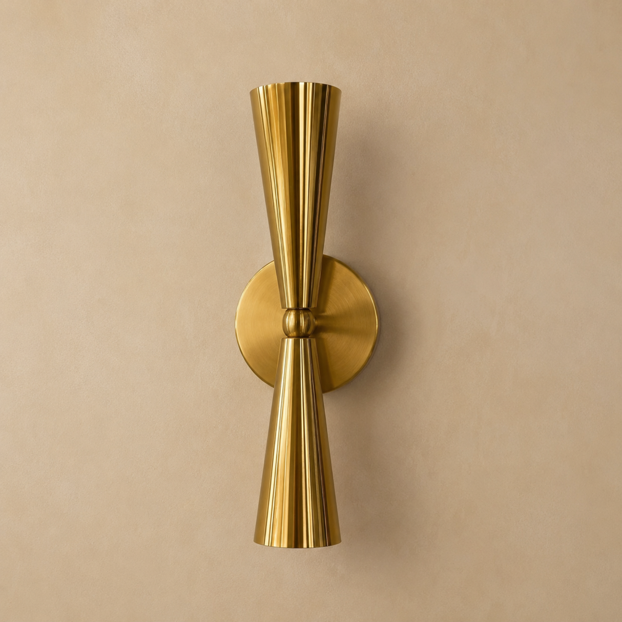 A modern brass wall sconce with a flared, ribbed cone design, mounted on a round circular backplate against a warm beige textured wall.