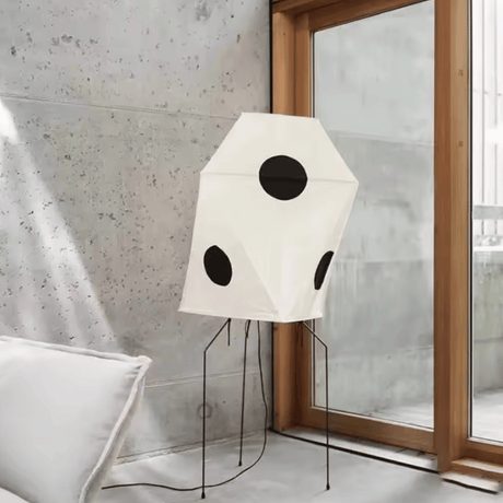 Modern floor lamp with geometric design in a room with a window and concrete wall.