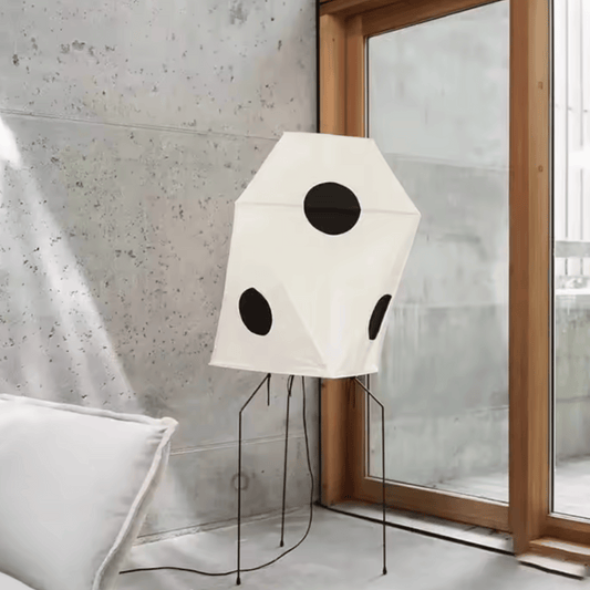 Modern floor lamp with geometric design in a room with a window and concrete wall.