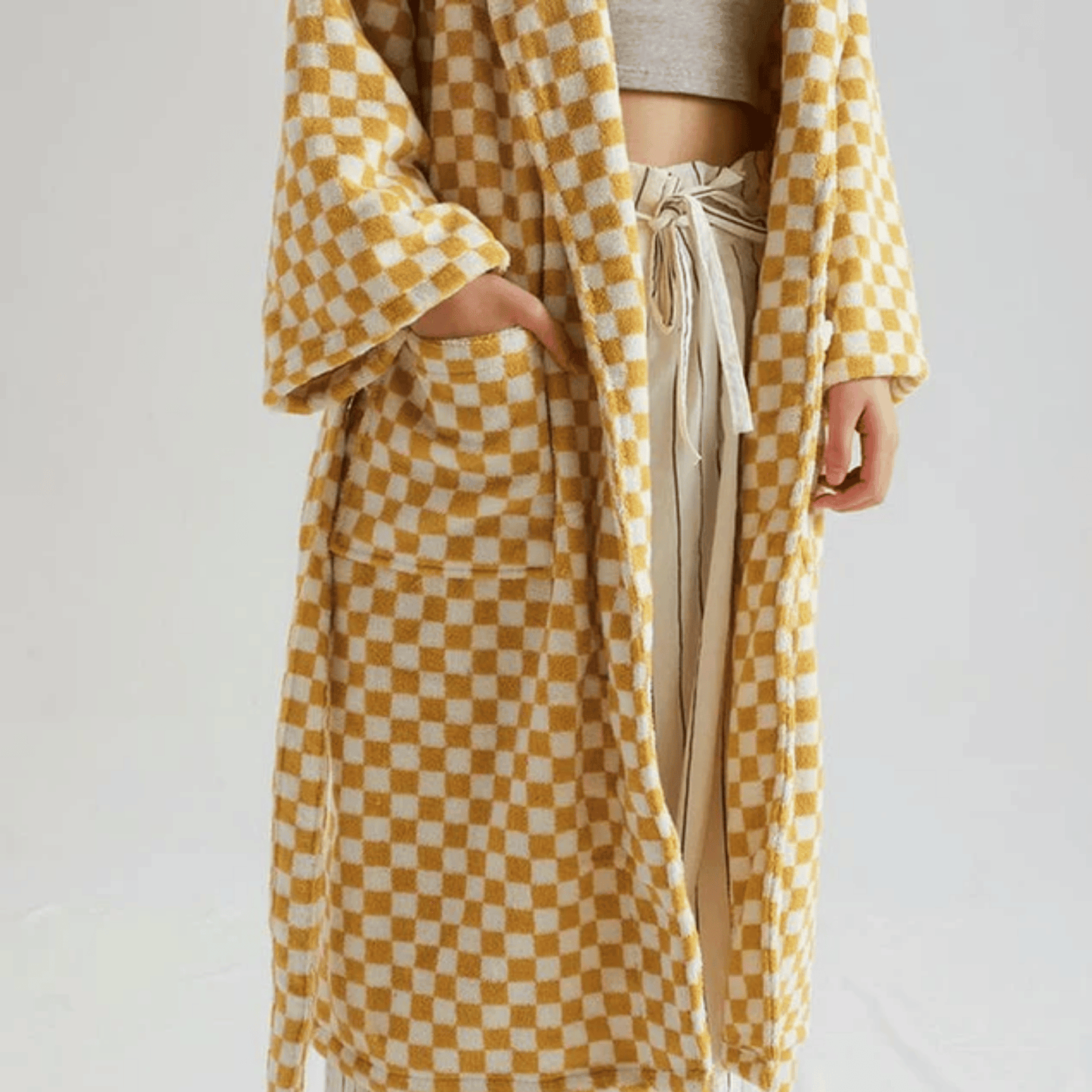 Person wearing a yellow and white checkered robe over a neutral outfit on a plain background