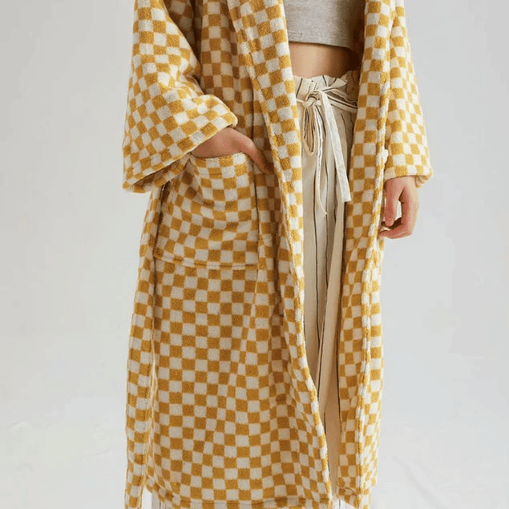 Person wearing a yellow and white checkered robe over a neutral outfit on a plain background