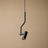 A modern black pendant light with a curved, bent metal arm and a cylindrical shade, shown hanging against a solid beige background.