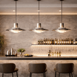 Modern bar setting with pendant lights, shelves of bottles, and chairs.