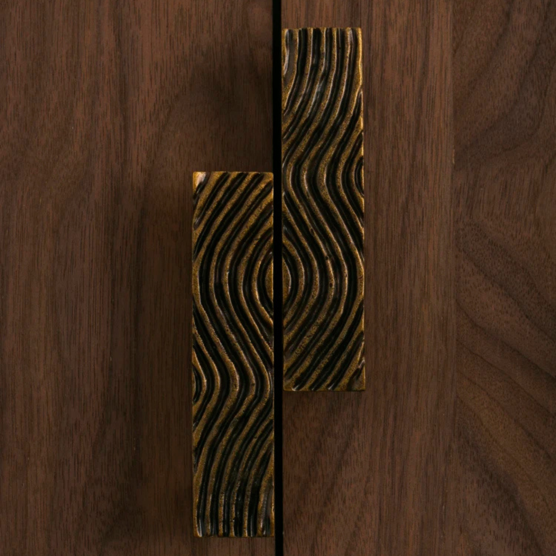 A pair of wave-patterned metal handles placed side by side on a wooden table.