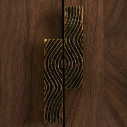 A pair of wave-patterned metal handles placed side by side on a wooden table.