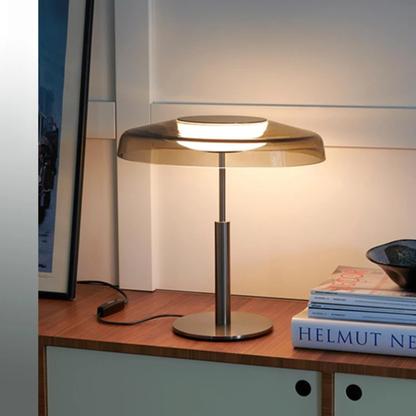 Another similar lamp on a desk, illuminated with a warm white light, next to a stack of books.