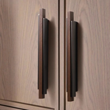Pair of long bronze and wood handles installed vertically on a light wooden cabinet door