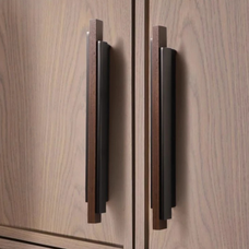 Pair of long bronze and wood handles installed vertically on a light wooden cabinet door