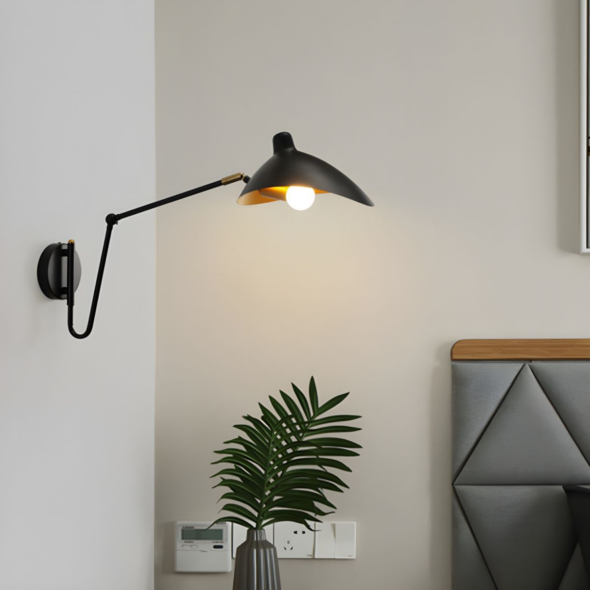 Gold and black adjustable wall lamp mounted near a wooden headboard, creating a cozy ambient glow.