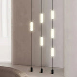 Multiple vertical tube pendant lights hanging in a row from the ceiling, casting warm light in a modern interior.