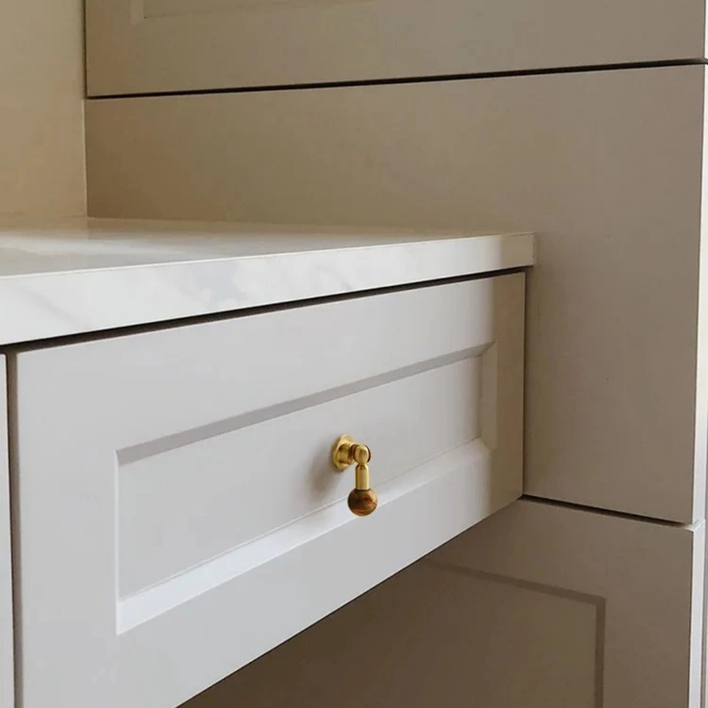 White drawer featuring a brass cabinet knob with a brown gemstone sphere handle.