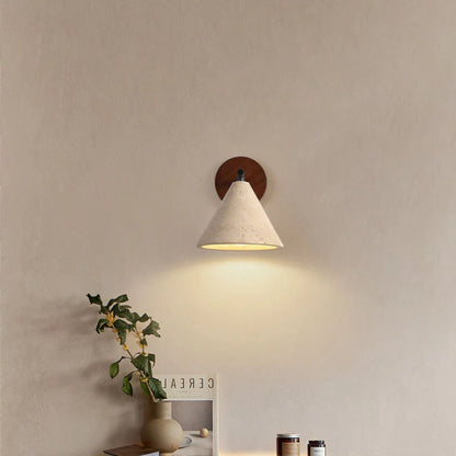 A wooden-backed wall lamp with a white cone shade glowing softly above a minimalist nightstand setup.