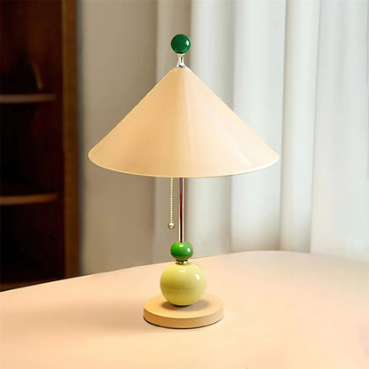 A side view of the table lamp with a cone-shaped beige shade, wooden base, and colorful green accents, placed on a simple surface.