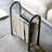 A tall, white leather and metal magazine holder standing upright on a soft gray carpet next to a sofa.
