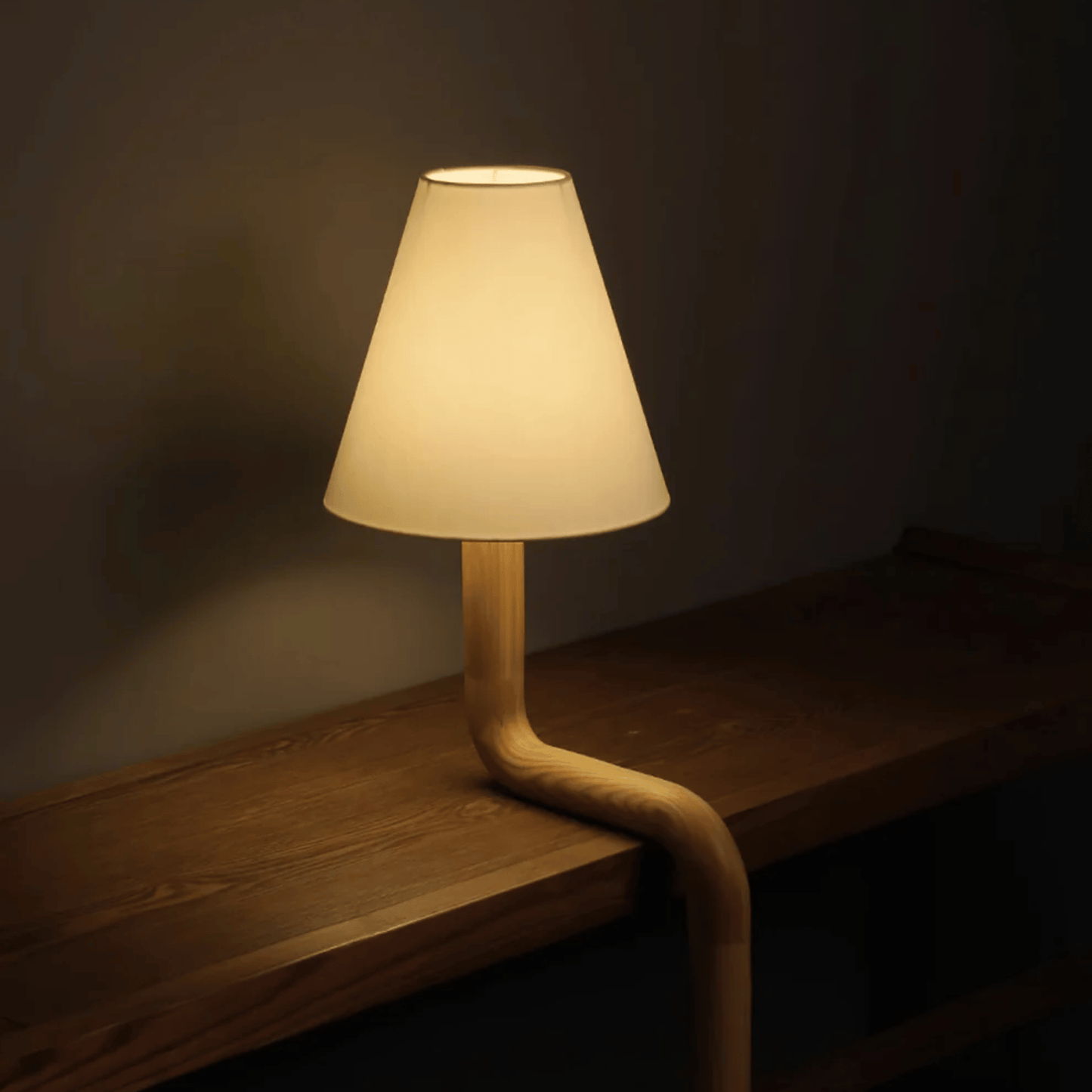 Table lamp with a unique弯曲设计 on a wooden surface in a dimly lit room.