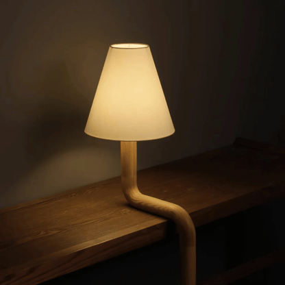 Table lamp with a unique弯曲设计 on a wooden surface in a dimly lit room.