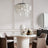 A minimalist dining space with a round white table, beige chairs, a decorative vase, and a stylish pendant light overhead.