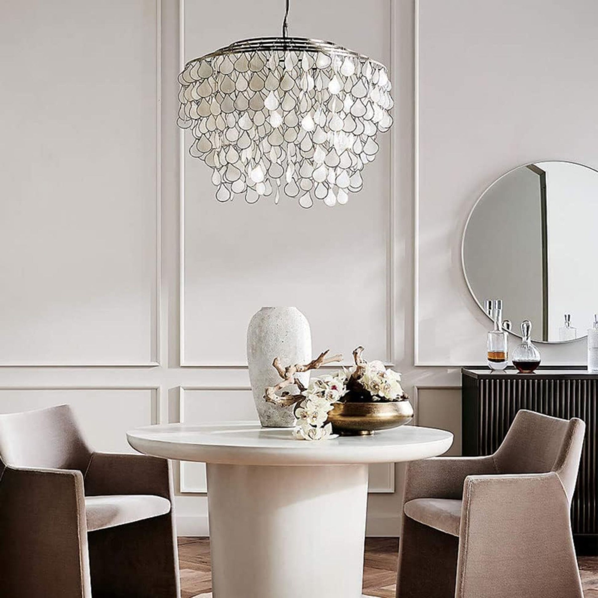 A minimalist dining space with a round white table, beige chairs, a decorative vase, and a stylish pendant light overhead.