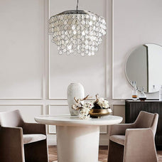 A minimalist dining space with a round white table, beige chairs, a decorative vase, and a stylish pendant light overhead.
