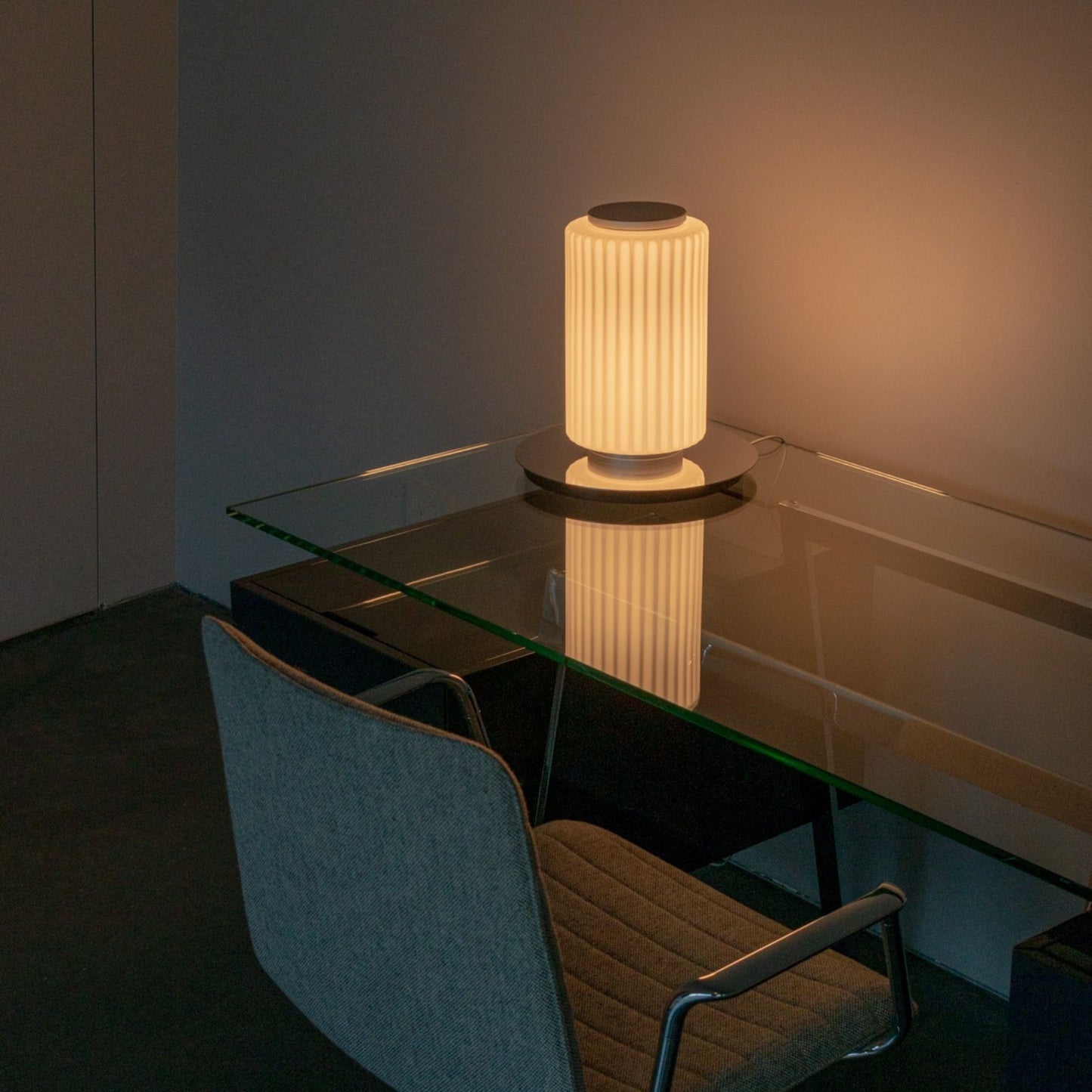 Two-tier ribbed-glass lamp illuminated on a round wooden side table near a window.