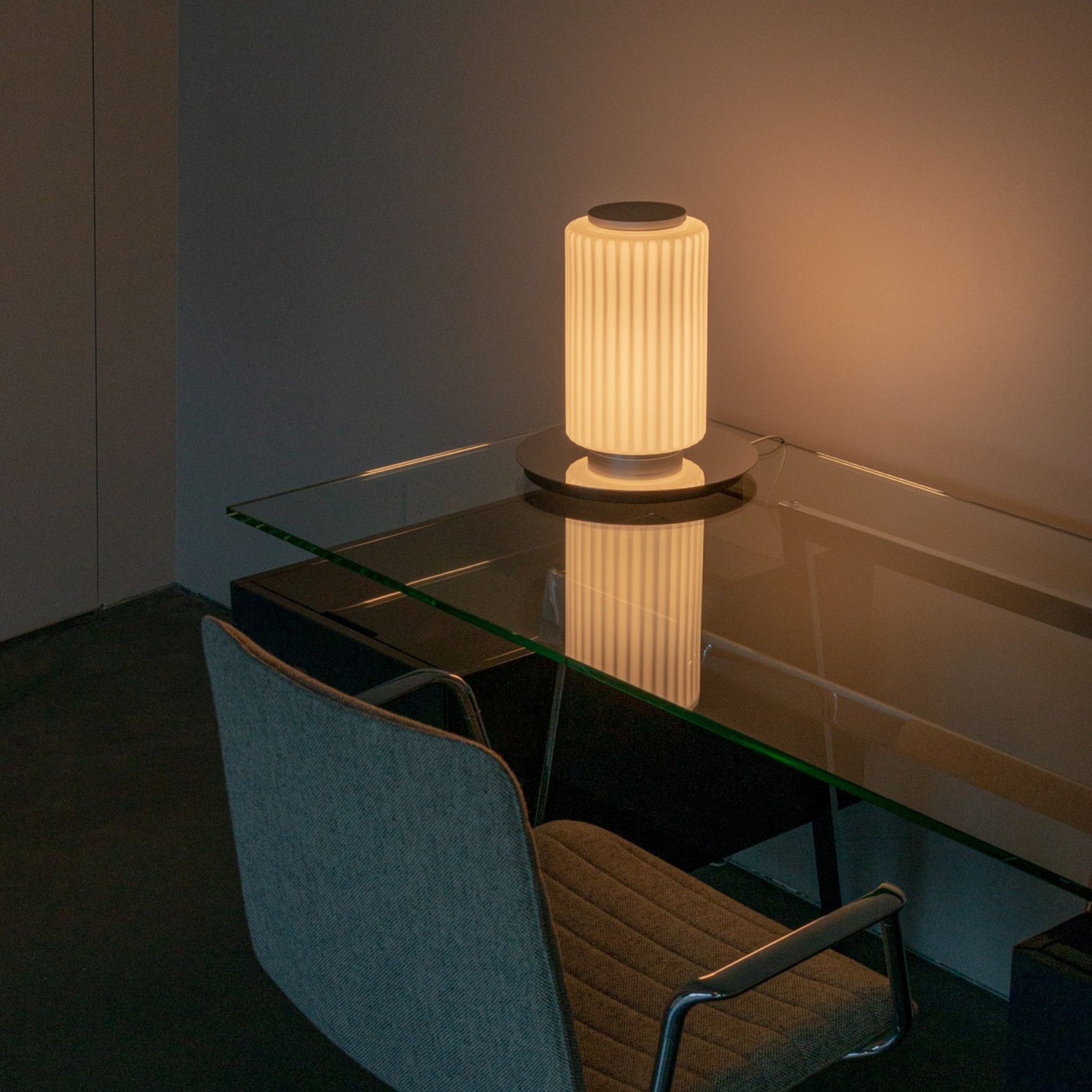 Two-tier ribbed-glass lamp illuminated on a round wooden side table near a window.