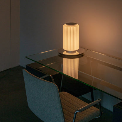Two-tier ribbed-glass lamp illuminated on a round wooden side table near a window.