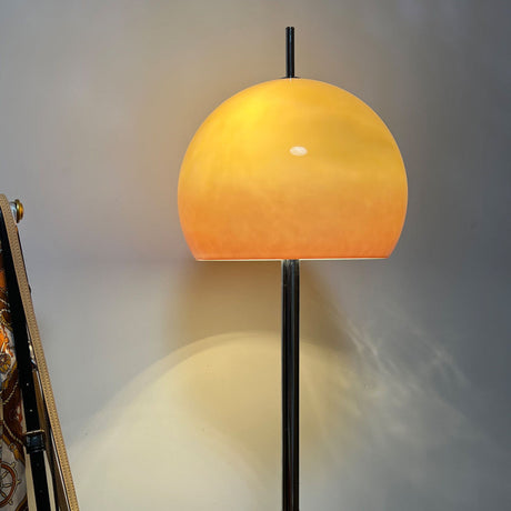 A floor lamp with a yellow globe-shaped shade standing next to a plant, creating a calm atmosphere in a living room.