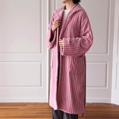 Person wearing a pink striped robe in a room with wooden flooring and white walls.