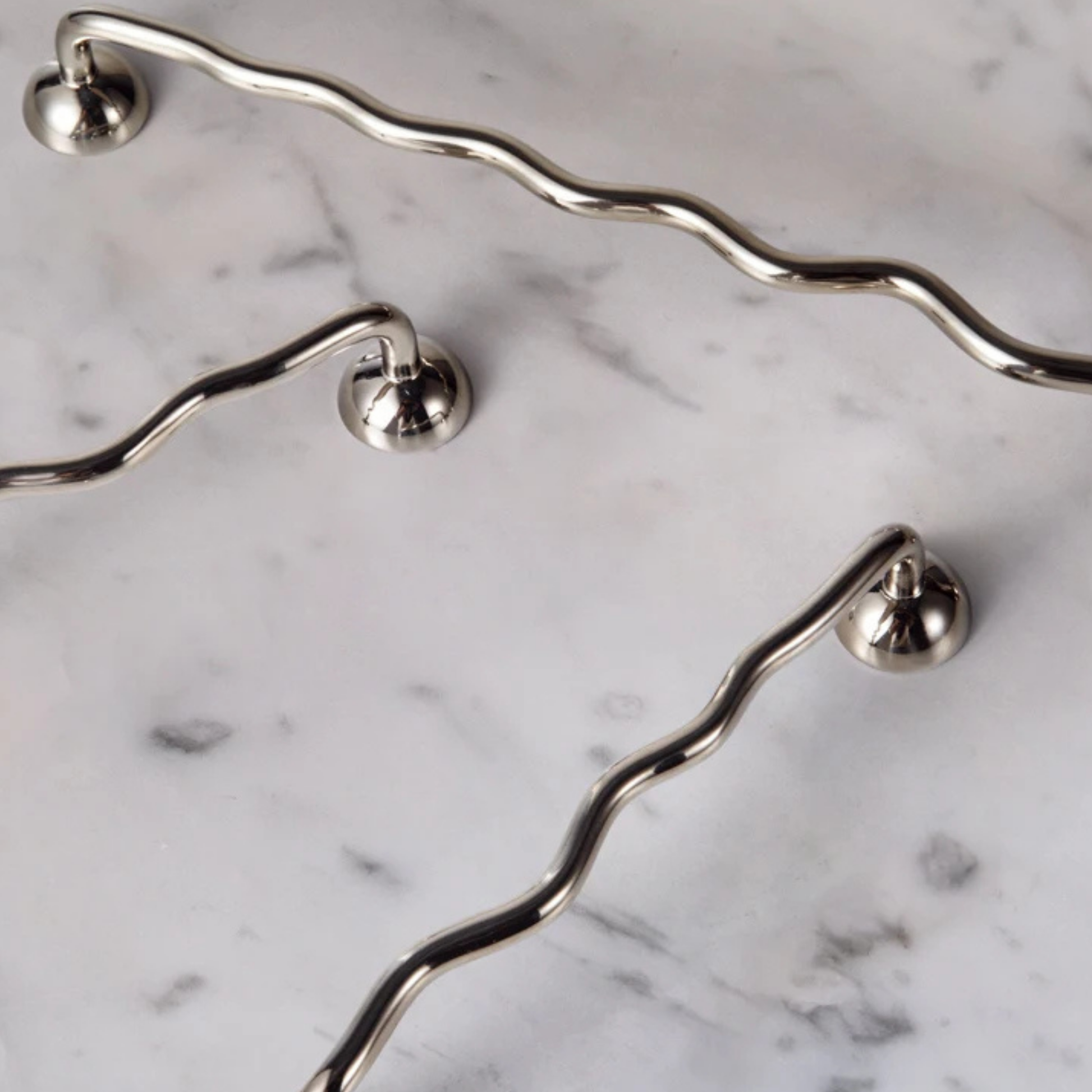 Set of wavy stainless steel handles displayed on a white marble surface