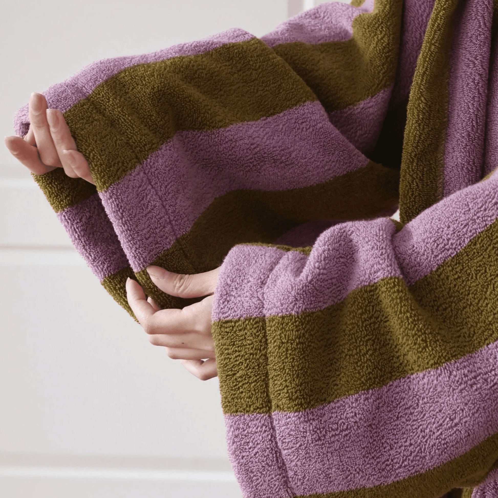 Close-up of hands holding a striped purple and green towel.
