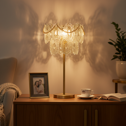 A dimly lit room showing a table with a decorative lamp in the foreground, with warm lighting casting shadows on the wall.