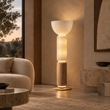 A modern two-tier floor lamp with a frosted white upper bowl and a natural wood lower cylinder, glowing with warm light in a contemporary living room setting.