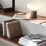 Books stacked on a wooden shelf with a lamp in the background