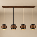 A four-light linear pendant ceiling fixture with dark wood shades, black metal accents, and warm glowing lights, suspended from a horizontal wooden bar against a beige wall.