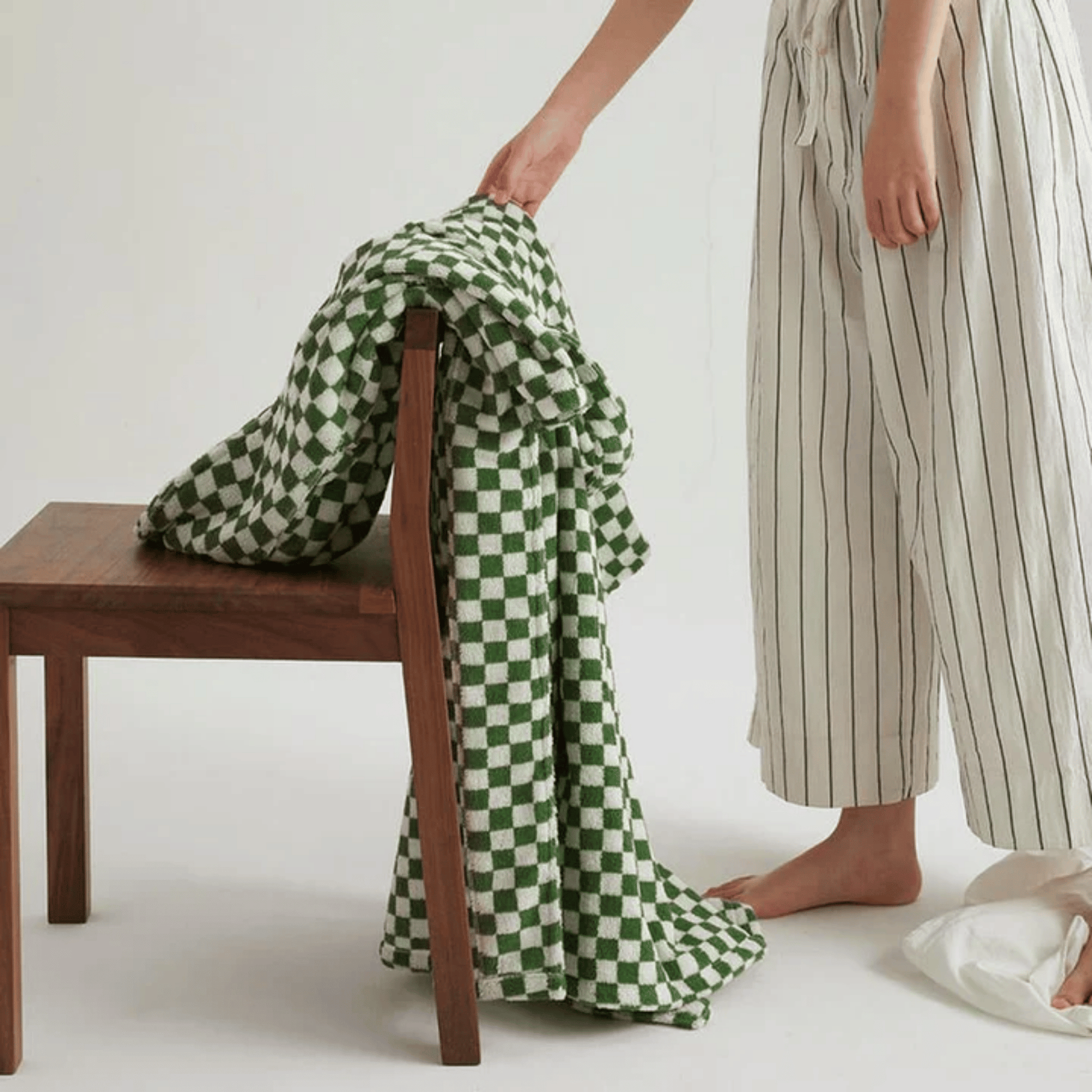 Person holding a green and white checkered blanket next to a wooden chair on a plain background