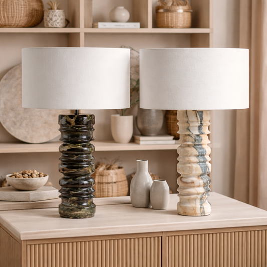 Two table lamps with marble bases on a wooden surface with decorative items in the background.