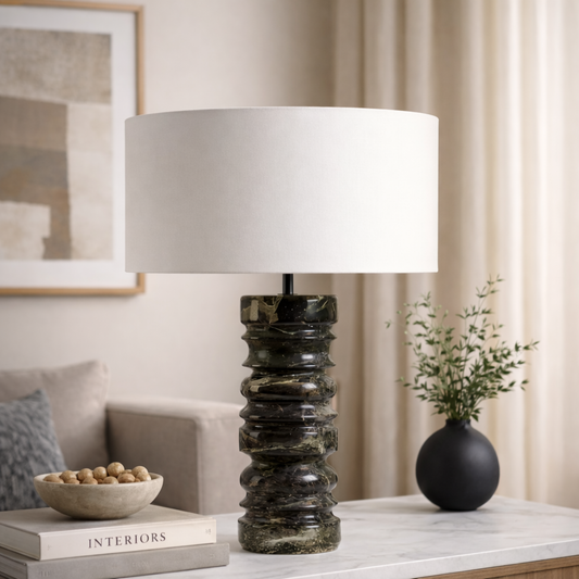 Decorative table lamp with a textured base on a surface with books and a vase in a room setting.