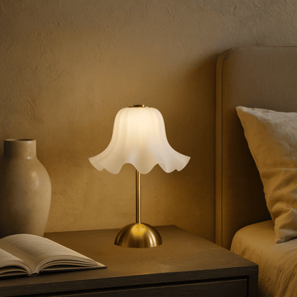 Table lamp on a nightstand next to an open book and a vase, with a warm glow.