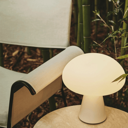 White table lamp on a table with a blurred background of greenery and furniture.