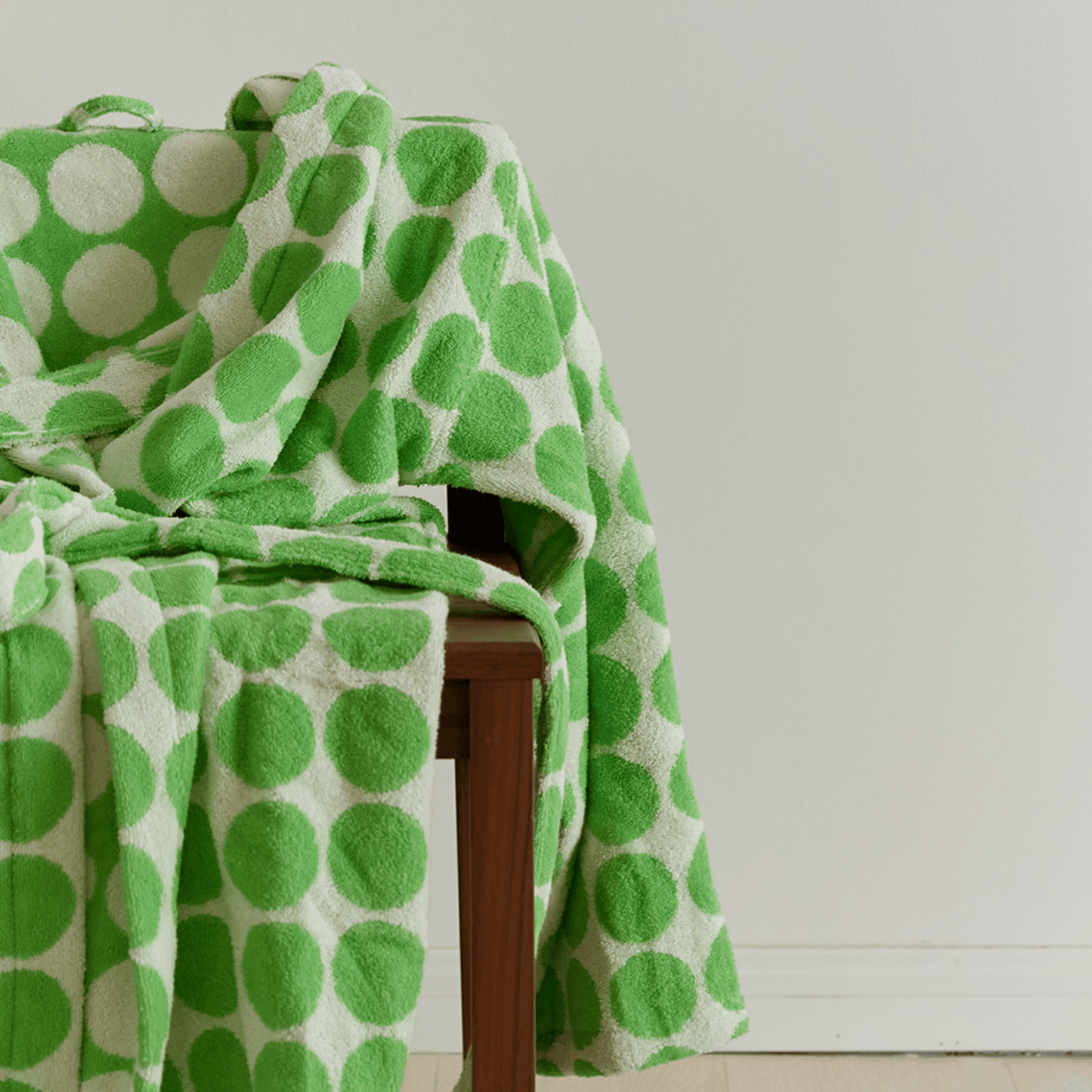 Green and white polka dot blanket draped over a wooden chair against a light background