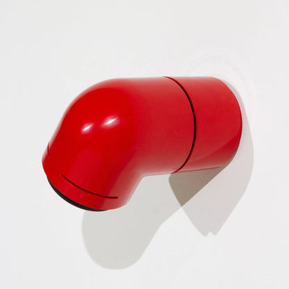 A red wall-mounted light fixture above a bed, casting a focused beam of light on a bedside table with books.
