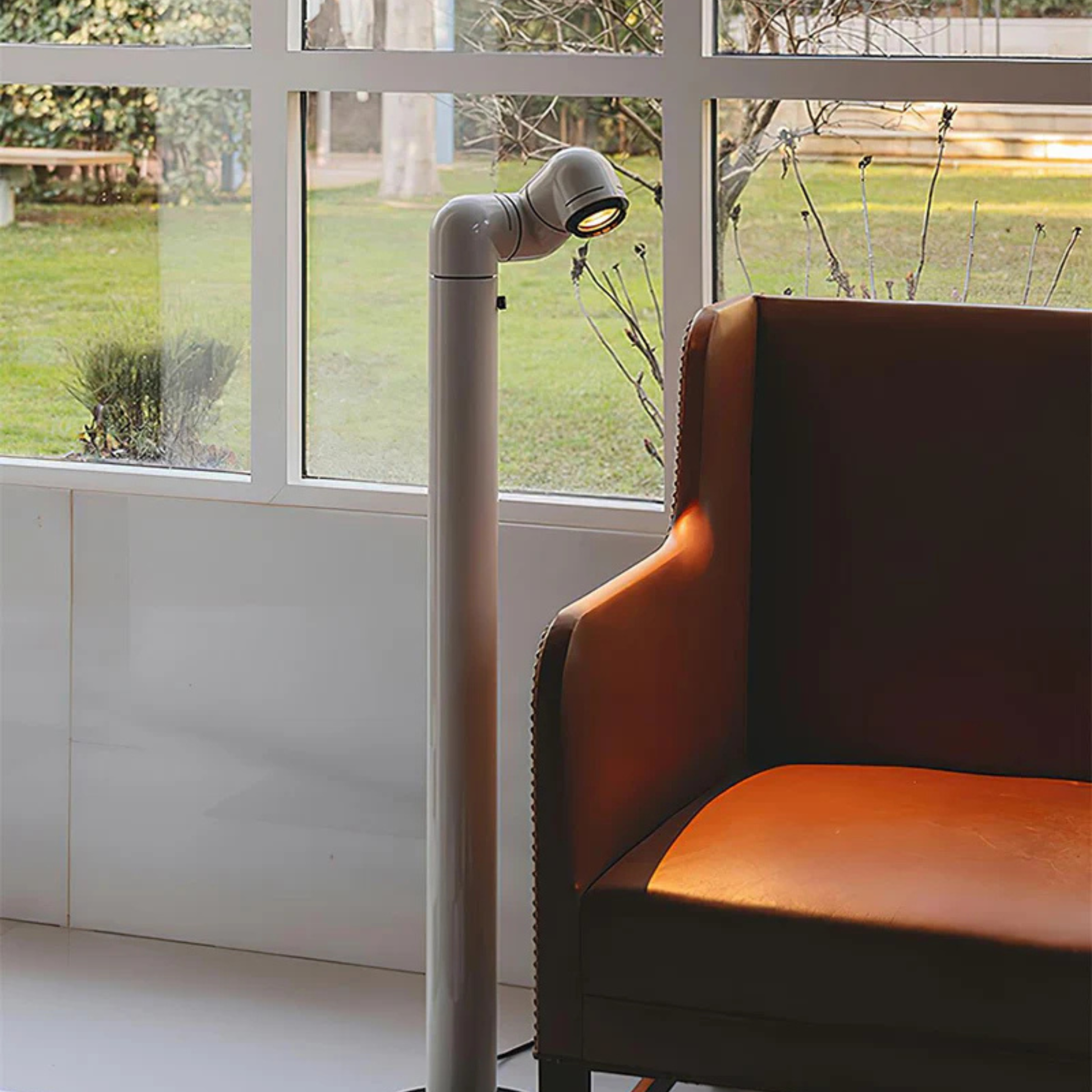 A white floor lamp with a sleek design, its light fixture angled to illuminate the space beside a chair.