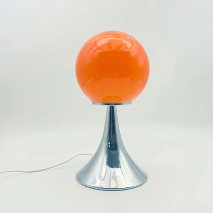 A bright orange glass globe table lamp with a chrome cone base placed on a white background.