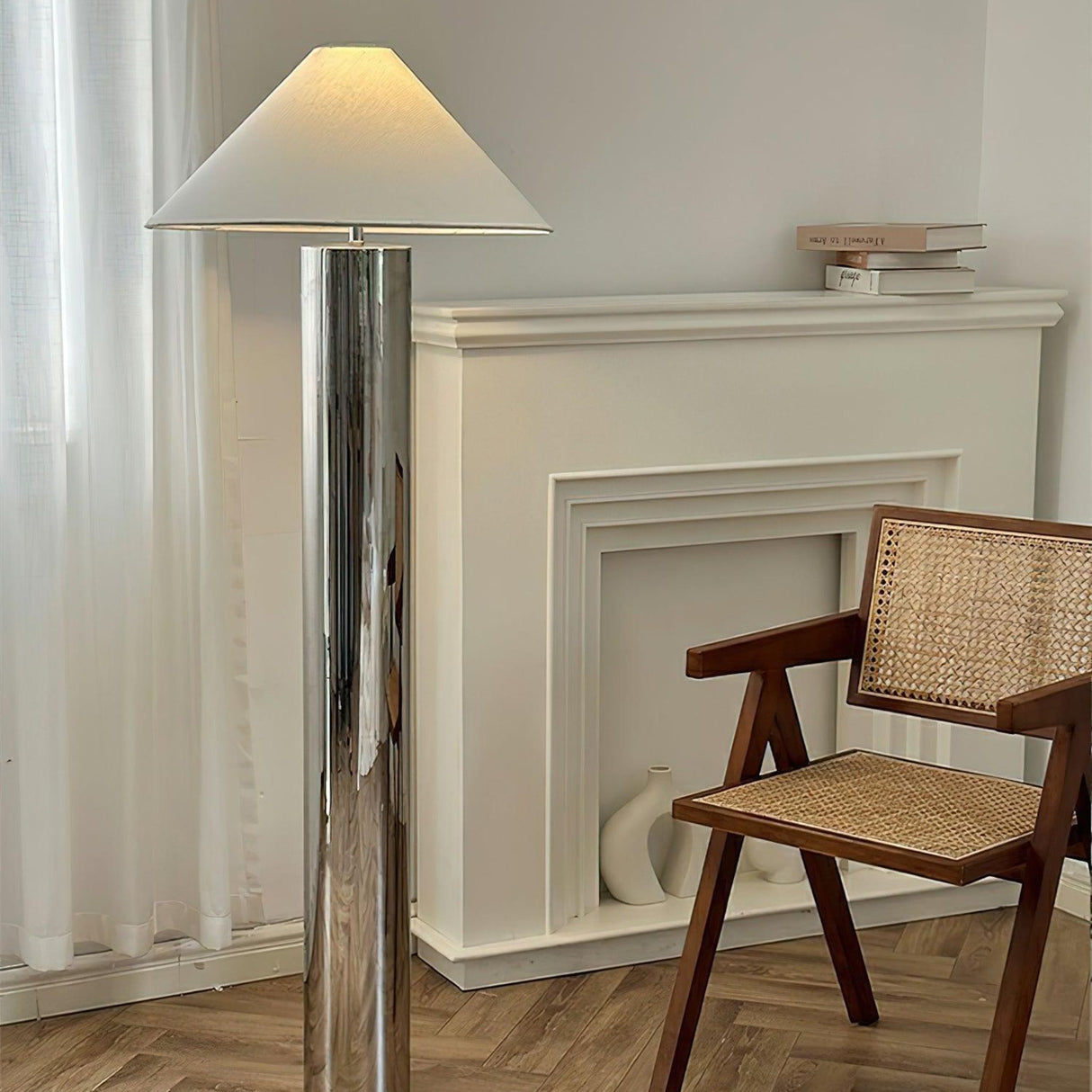 reflective chrome floor lamp beside a sofa with a white lampshade and indoor plants