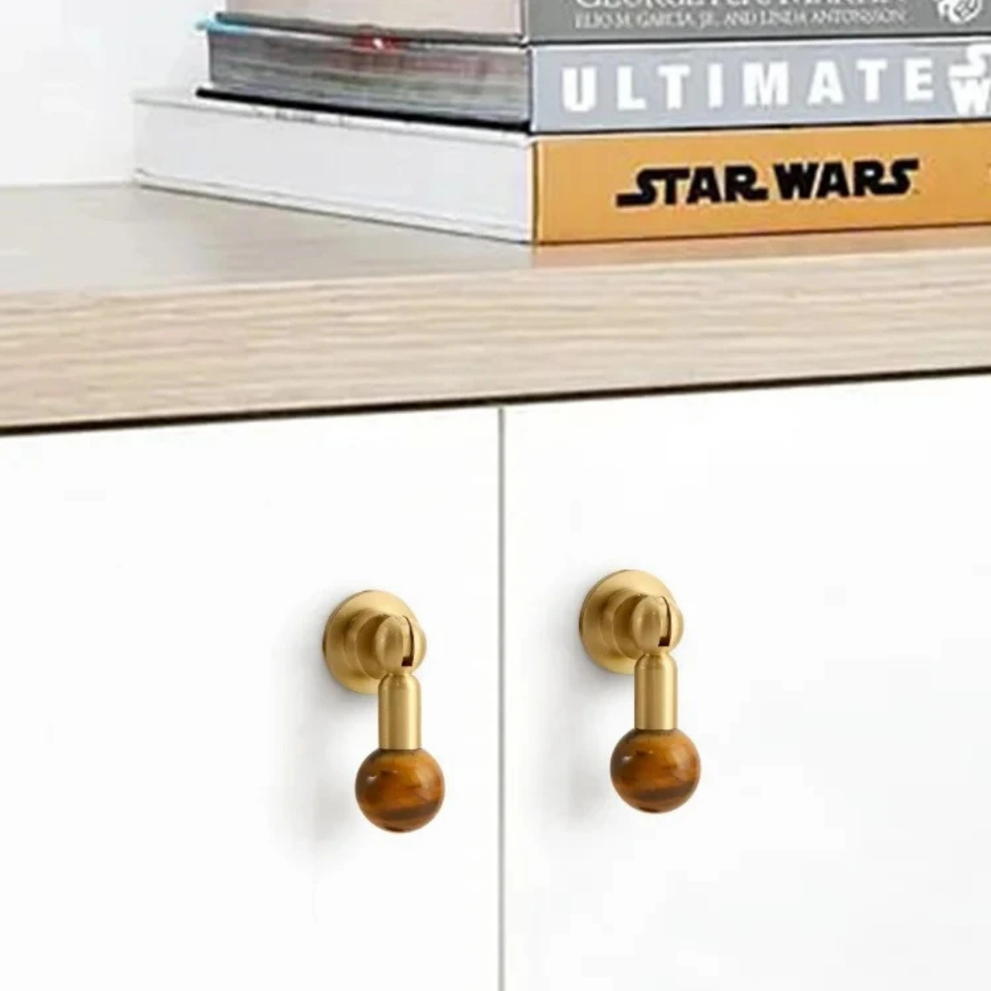Pair of brass cabinet knobs with brown gemstone sphere handles mounted on white cabinet doors.