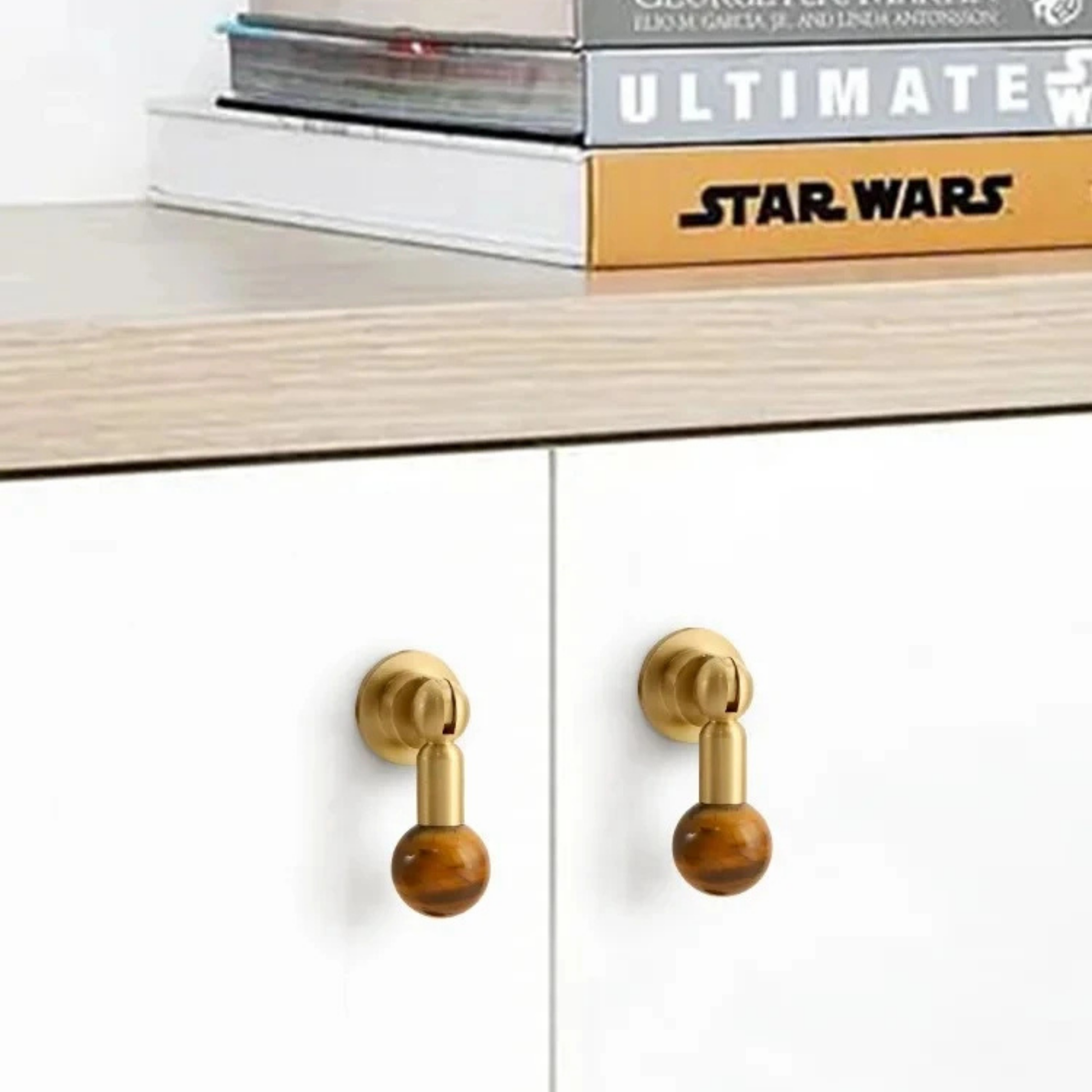 Pair of brass cabinet knobs with brown gemstone sphere handles mounted on white cabinet doors.