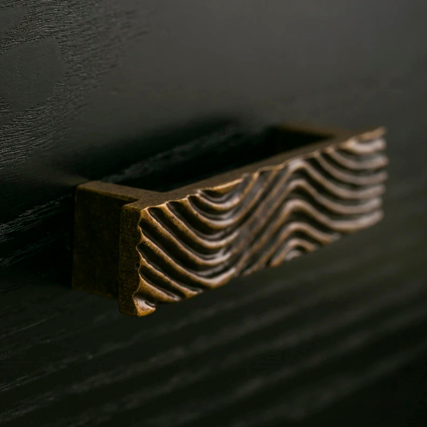 A close-up of a single textured brass handle installed on a dark wood drawer.