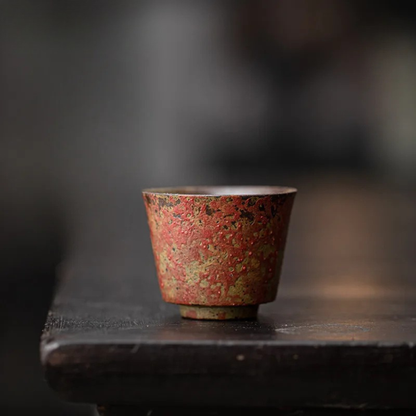 A single red textured ceramic tea cup displayed on a dark wooden surface.