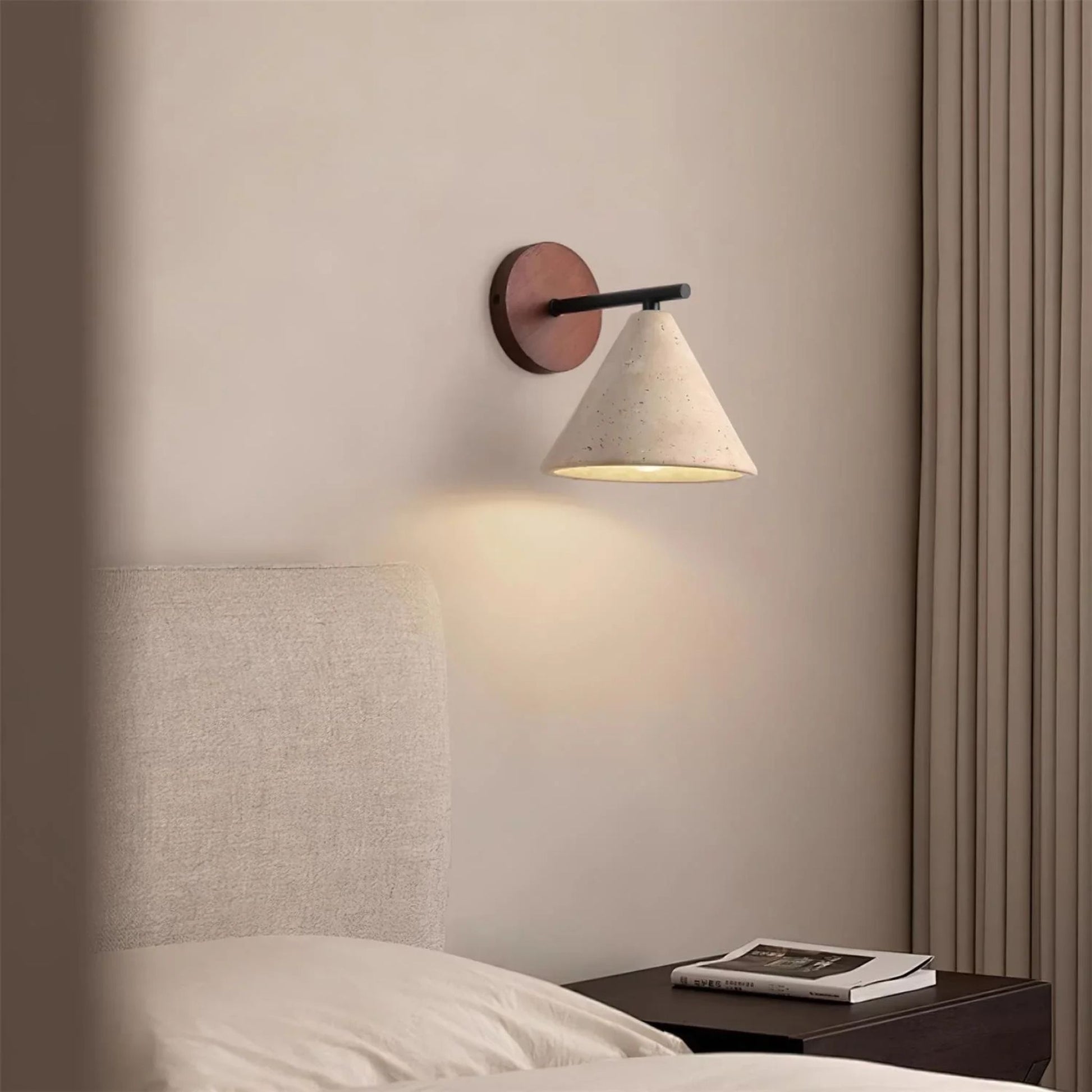 A wood and white cone-shaped wall sconce illuminating a neutral-toned bedroom, positioned above a bed.